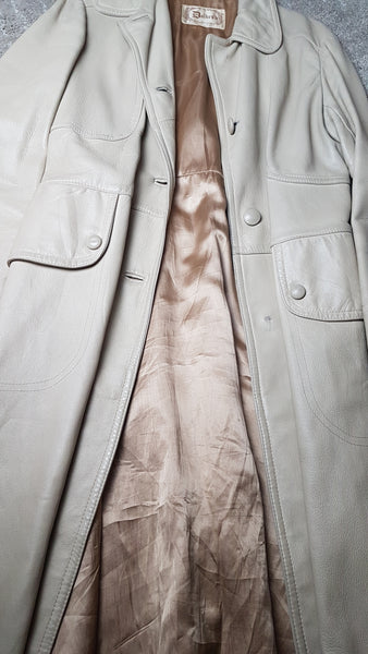Flatlay view of a vintage 1970s sand-coloured leather trench coat with tonal buttons, shoulder tabs and a matching belt