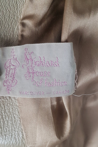 Highland House of Fashion label on flatlay view of a vintage 1970s sand-coloured leather trench coat with tonal buttons, shoulder tabs and a matching belt