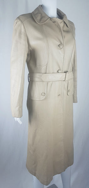 Side three-quarter view of a vintage 1970s sand-coloured leather trench coat with tonal buttons, shoulder tabs and a matching belt displayed on a mannequin