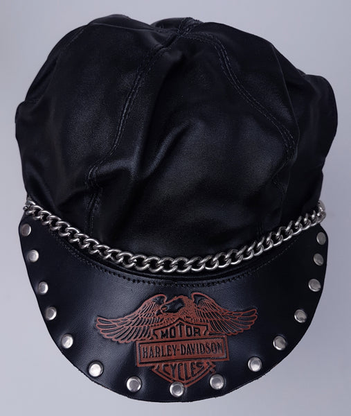 Front view showing the panelled black crown, chain trim and red-orange emblem across the studded peak