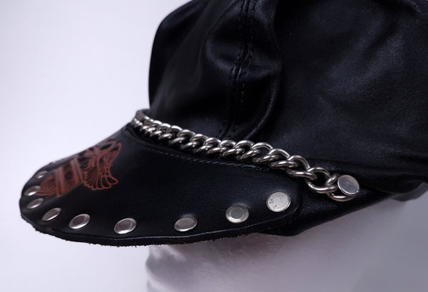 Side close-up showing the red-orange Harley-Davidson emblem and the studded peak and silver-tone chain extending around the cap