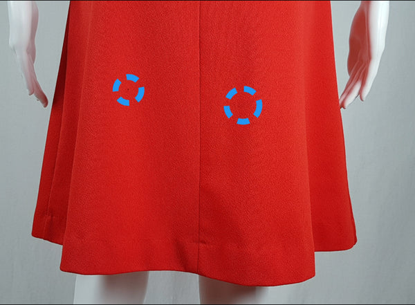 Flaws circled to show 2 small penmarks on a close up back hemline view of a vintage 1970s Kenny Classics Donnkenny orange-red mod dress  on a mannequin