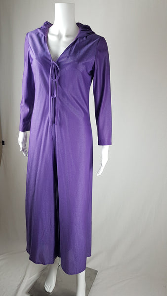 three quarter view of a 1970s Nu-Mode purple jumpsuit with a draped hood, V-neckline, front zip and ties, long sleeves and wide legs displayed on a mannequin 