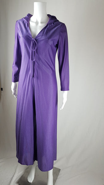 three quarter view of a 1970s Nu-Mode purple jumpsuit with a draped hood, V-neckline, front zip and ties, long sleeves and wide legs displayed on a mannequin 