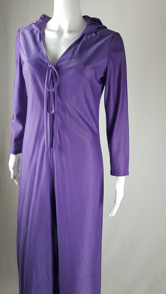 three quarter view of a 1970s Nu-Mode purple jumpsuit with a draped hood, V-neckline, front zip and ties, long sleeves and wide legs displayed on a mannequin 
