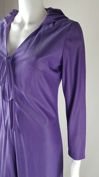 three quarter view of a 1970s Nu-Mode purple jumpsuit with a draped hood, V-neckline, front zip and ties, long sleeves and wide legs displayed on a mannequin 
