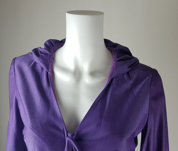 Front shoulders view of a 1970s Nu-Mode purple jumpsuit with a draped hood, V-neckline, front zip and ties, long sleeves and wide legs displayed on a mannequin 