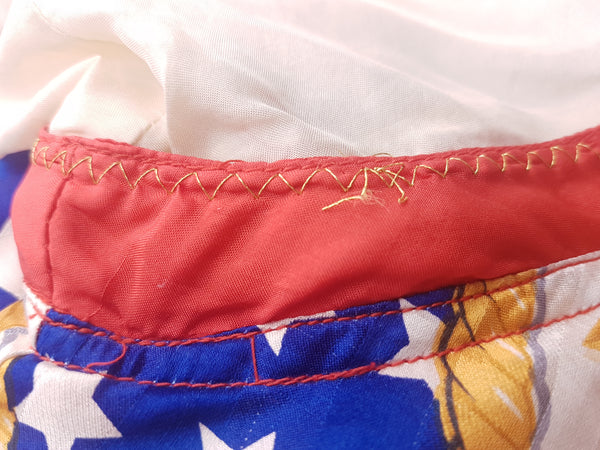 Close-up of the red-trimmed detachable sleeves, some fabric and stitching abrasions and bold USA flag, star and gold-chain print on a vintage 1980s - 1990s Mureli silk bomber jacket.