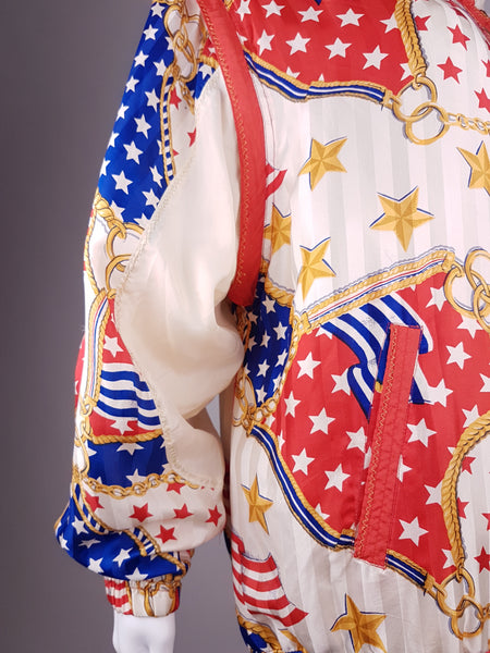 Closeup sleeve and back view of a Vintage 1980s - 1990s  Mureli silk bomber jacket with a red, white, blue and gold USA flag and chain print, detachable sleeves, red trim and an oversized blouson silhouette, displayed on a mannequin