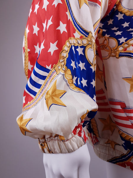 Closeup sleeve and elasticated cuff view of a Vintage 1980s - 1990s  Mureli silk bomber jacket with a red, white, blue and gold USA flag and chain print, detachable sleeves, red trim and an oversized blouson silhouette, displayed on a mannequin