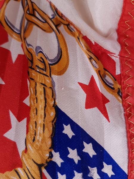 Close-up view of a minor fabric abrasion and the bold USA flag, star and gold-chain print on a vintage 1980s - 1990s Mureli silk bomber jacket.