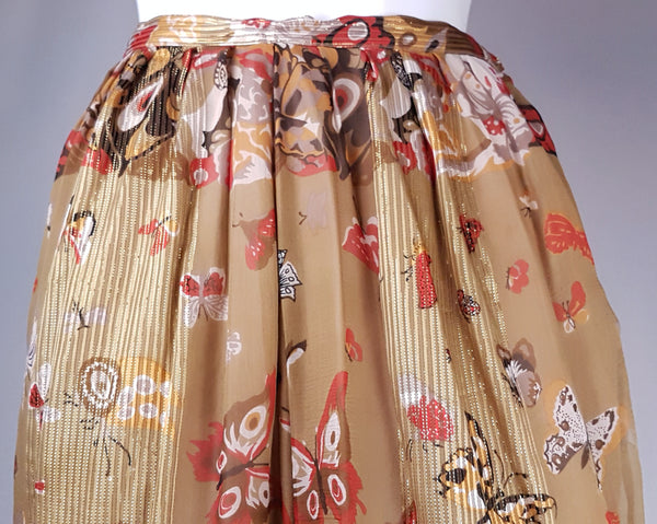 Close-up of the trouser waistband, gathered upper section and fine vertical metallic stripes in the printed silk.