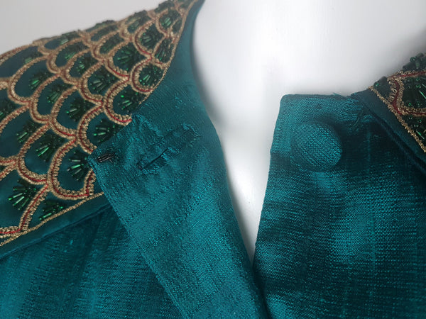 Close-up of the jacket neckline showing the pointed beaded collar and upper fabric-covered loop-button fastening.
