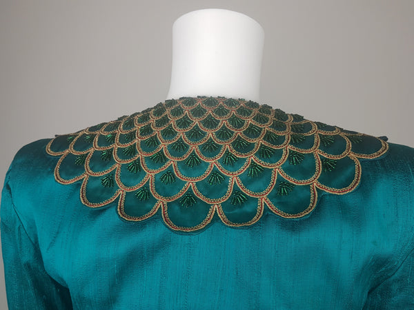 Back close-up of the broad collar embellished with layered scallops, metallic-gold braid, fine red cord and emerald-green beads.