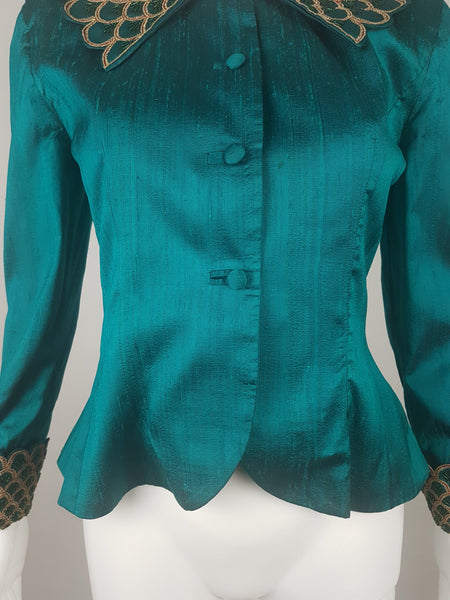 Closer front view of a fitted teal silk Spaghetti London jacket showing its fabric-covered loop buttons, shaped seams and flared lower hem.