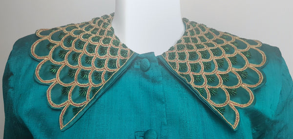 Front close-up of the broad pointed collar embellished with layered scallops, metallic-gold braid, fine red cord and emerald-green beads.
