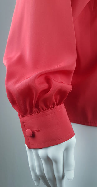 Closeup view of sleeve, cuff and button on a vintage 1980s St Michael red pussy-bow blouse with stitched front pleats, fabric-covered buttons and gathered long sleeves displayed on a mannequin 