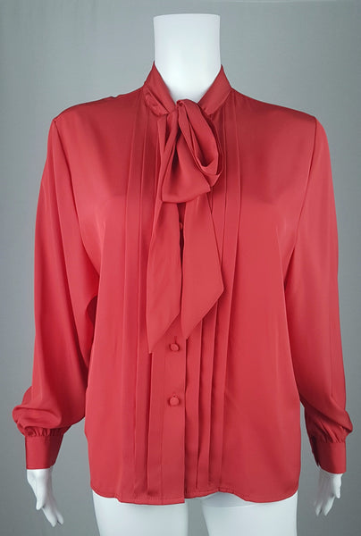 Front view of a vintage 1980s St Michael red pussy-bow blouse with stitched front pleats, fabric-covered buttons and gathered long sleeves displayed on a mannequin 
