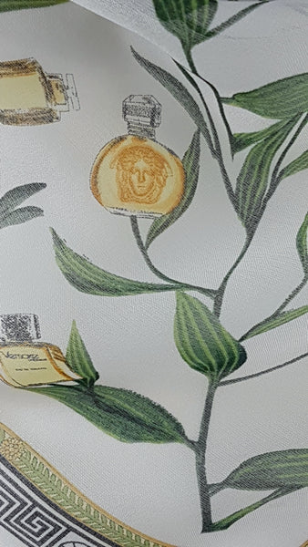 Close-up of green botanical branches and gold Versace perfume bottles, including a round Medusa-head bottle, printed on ivory chiffon.