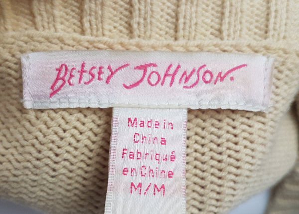 Close-up view of the white and pink Betsey Johnson label and size tag marked M/M and Made in China on a vintage 2000s sand-beige Betsey Johnson cropped cardigan