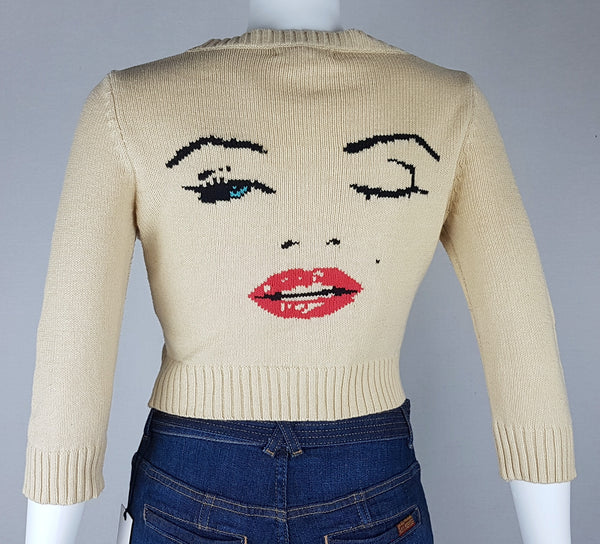Full back view of a vintage 2000s sand-beige Betsey Johnson cropped cardigan with three-quarter sleeves, cropped ribbed hem and with an intarsia Marilyn Monroe wink portrait in black, blue, red and white displayed on a mannequin