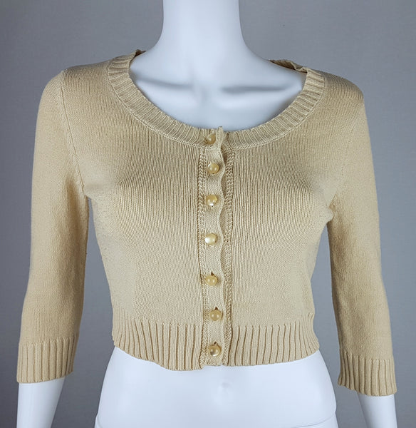 Full front view of a vintage 2000s sand-beige Betsey Johnson cropped cardigan with three-quarter sleeves, pearl-effect buttons and a cropped ribbed hem displayed on a mannequin