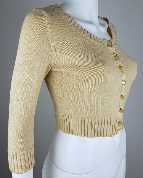 Three-quarter front view of a vintage 2000s sand-beige Betsey Johnson cropped cardigan with three-quarter sleeves, pearl-effect buttons and a cropped ribbed hem displayed on a mannequin