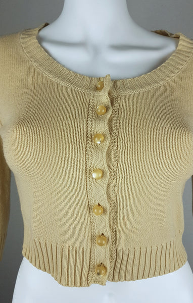 Close-up view of the pearl-effect buttons and wide ribbed hem on a vintage 2000s sand-beige Betsey Johnson cropped cardigan displayed on a mannequin