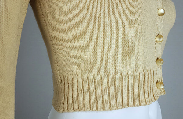 Close-up side view of the pearl-effect buttons and wide ribbed hem on a vintage 2000s sand-beige Betsey Johnson cropped cardigan displayed on a mannequin