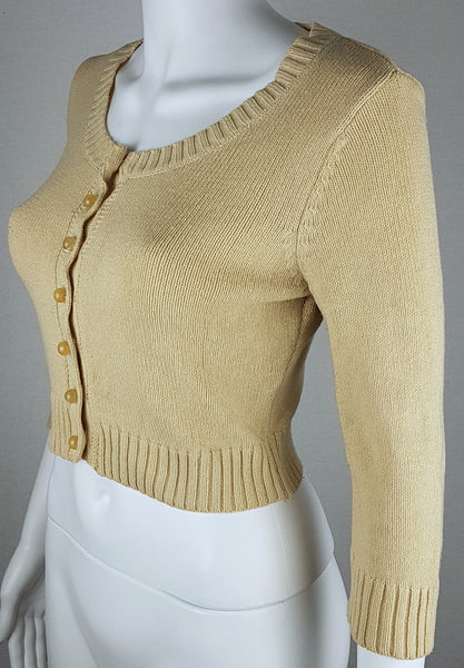 Three-quarter front view of a vintage 2000s sand-beige Betsey Johnson cropped cardigan with three-quarter sleeves, pearl-effect buttons and a cropped ribbed hem displayed on a mannequin
