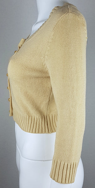 Side view of a vintage 2000s sand-beige Betsey Johnson cropped cardigan with three-quarter sleeves, pearl-effect buttons and a cropped ribbed hem displayed on a mannequin