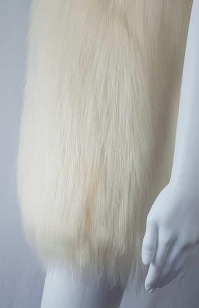 Close up view of a patch of color variation in a cream long-pile faux-fur vest with a collarless neckline, decorative fastening and side pockets displayed on a mannequin