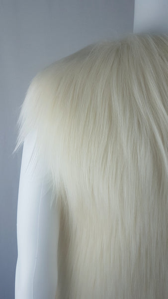 Close up back shoulder view of a cream long-pile faux-fur vest with a collarless neckline displayed on a mannequin