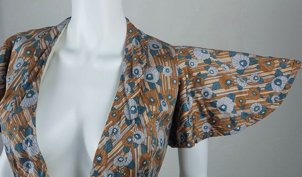 outstretched sleeve closeup view of a vintage late 1950s dressmaker-made Vogue Couturier Design tunic top in a tan and blue abstract floral print, with circular cape sleeves and a fitted waist displayed on a mannequin 
