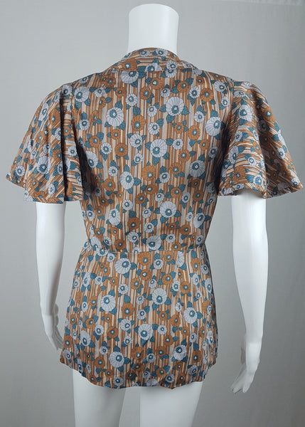 back view of a vintage late 1950s dressmaker-made Vogue Couturier Design tunic top in a tan and blue abstract floral print, with circular cape sleeves and a fitted waist displayed on a mannequin 