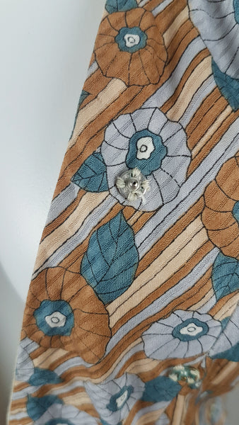snap closure detail view of a vintage late 1950s dressmaker-made Vogue Couturier Design tunic top in a tan and blue abstract floral print, with circular cape sleeves and a fitted waist displayed on a mannequin 