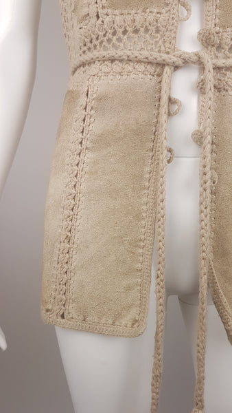 Lower front view of the suede vest worn open, showing its crochet-edged panels and braided tie belt.