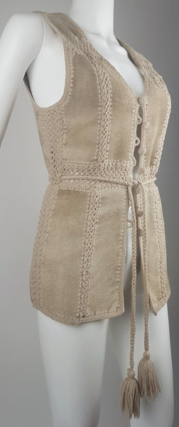 Three-quarter side view of a vintage 60s - 70s Hudson Bay Company sand-beige suede vest with crochet panel joins and a long tassel tie belt.