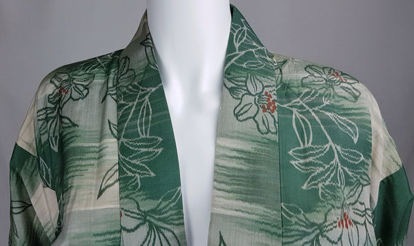 Close-up of the neckline and shoulders of a vintage green silk kimono with ivory flowers and rust-red accents.