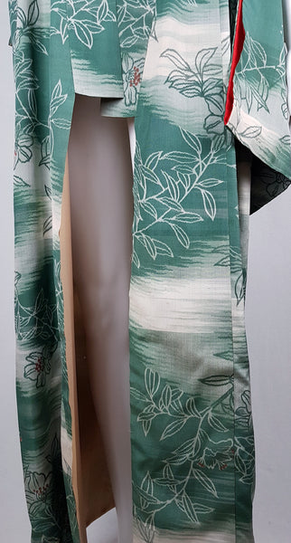 Lower front view of an open green floral silk kimono showing its overlapping panels and pale interior lining.