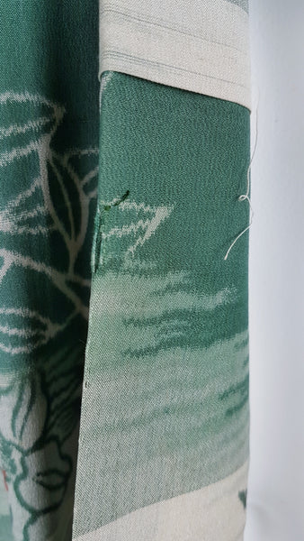Condition close-up showing a small hole and loose thread near the edge of a green silk kimono panel.