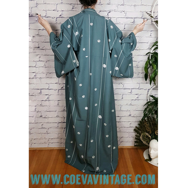 Woman modelling a blue grey kimono robe with wide sleeves, white stripes and floral medallions - back view