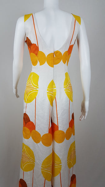 Vintage 1960s white palazzo jumpsuit on a mannequin with a V-neck and bold orange and yellow abstract print - back view