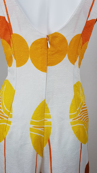 Vintage 1960s white palazzo jumpsuit on a mannequin with a V-neck and bold orange and yellow abstract print - back zipper details