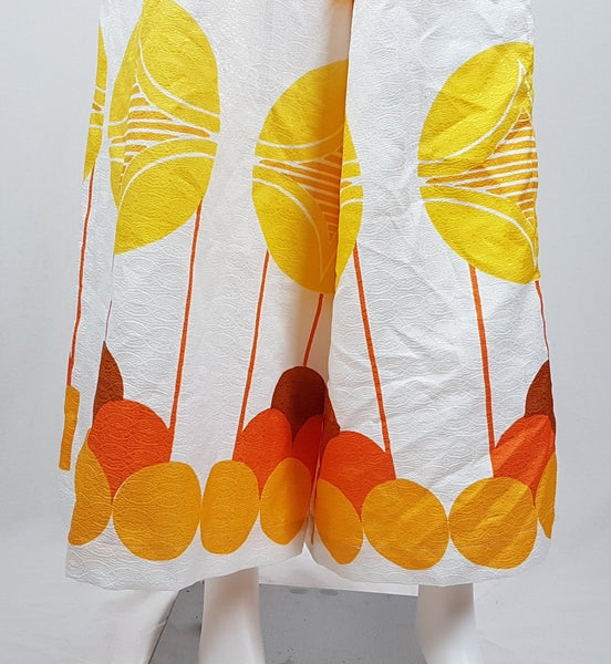 Vintage 1960s white palazzo jumpsuit on a mannequin with a V-neck and bold orange and yellow abstract print - trouser hem view