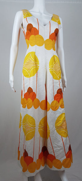 Vintage 1960s white palazzo jumpsuit on a mannequin with a V-neck and bold orange and yellow abstract print - front view