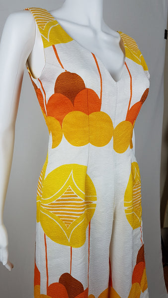Vintage 1960s white palazzo jumpsuit on a mannequin with a V-neck and bold orange and yellow abstract print - bust and waist view