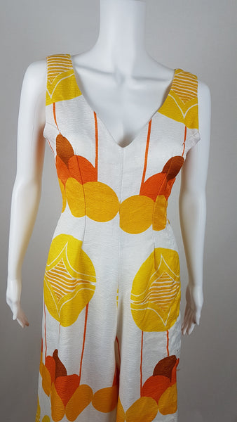 Vintage 1960s white palazzo jumpsuit on a mannequin with a V-neck and bold orange and yellow abstract print - bust and waist view