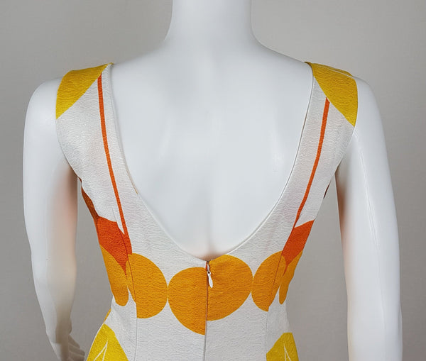 Vintage 1960s white palazzo jumpsuit on a mannequin with a V-neck and bold orange and yellow abstract print - back view