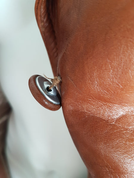 Reverse of a leather-covered button showing its metal shank and frayed attachment thread